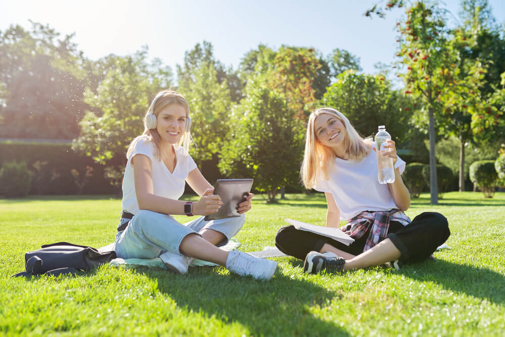 Študentki na lep sončen dan sedita na travniku in pijeta vodo